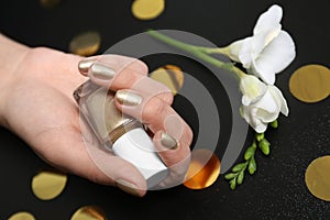 Woman with golden manicure holding nail polish bottle on black background