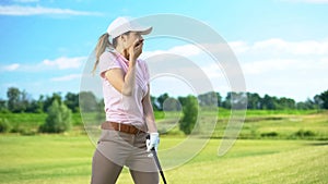 Woman with golf club closing mouth by hand, shocked with failed shot, loser