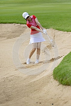 Woman golfer hitting golf ball in sand trap