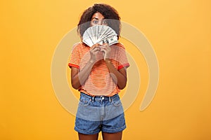 Woman gonna waste lots of cash today. Pleased and delighted rich african american girl with curly hairstyle hiding face