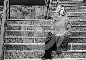 Woman with gorgeous hairstyle sit on stairs outdoors. Fall fashion trend. Layer oversize knit over girly skirt. Wearable