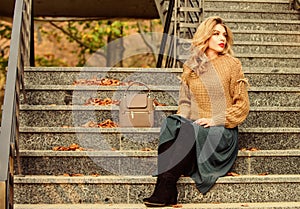 Woman with gorgeous hairstyle sit on stairs outdoors. Fall fashion trend. Layer oversize knit over girly skirt. Wearable