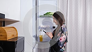 Woman in gown opens door of refrigerator to check products