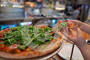 Woman grabbing slice of pizza with arugula greens on top