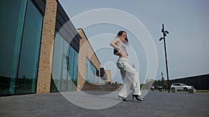 Woman gracefully dancing in high heels in front of urban building. Energetic woman performing dance routine outdoors.