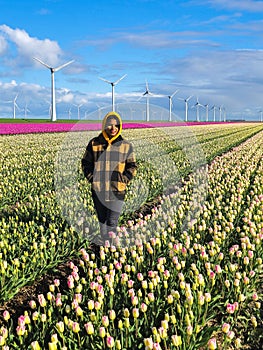 A woman gracefully stands in a vibrant field of tulips, surrounded by bursts of colorful petals under the Dutch windmill