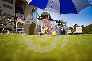 Woman on the grass, looking at the laptop under umbrella near th