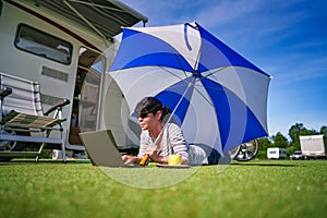 Woman on the grass, looking at the laptop under umbrella near th