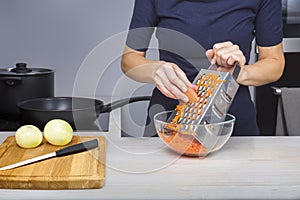 A woman grates carrots into a glass bowl while cooking soup in her kitchen