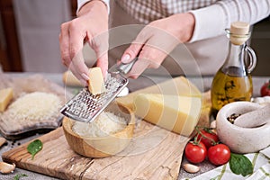 Woman grates Parmesan cheese on a wooden cutting board at domestic kitchen