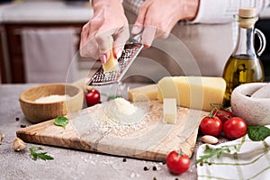 Woman grates Parmesan cheese on a wooden cutting board at domestic kitchen