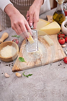 Woman grates Parmesan cheese on a wooden cutting board at domestic kitchen