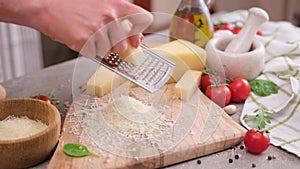 woman grates piece of parmesan hard cheese on a grater at domestic kitchen