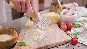 woman grates piece of parmesan hard cheese on a grater at domestic kitchen