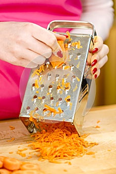 Woman grating carrot on metal grater