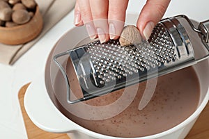 Woman grating nutmeg into cacao at table, closeup