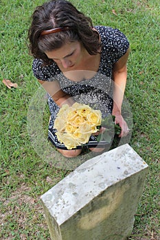 Woman at grave stone with yellow flowers.
