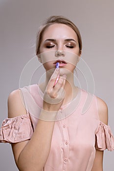 Woman on a gray background paints lips with lipstick.