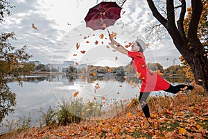 A woman in a gray beret, brunette with long hair, in a red dress holds an umbrella high above her head, maple leaves are