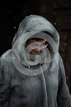 woman in a gray fur coat with a hood and red gloves poses for the camera.