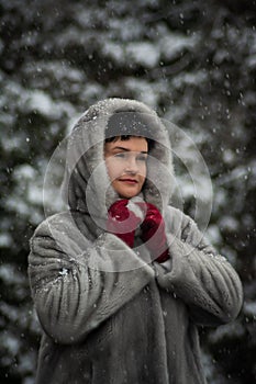 woman in a gray fur coat with a hood and red gloves poses for the camera.