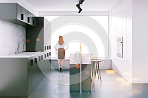 Woman in gray loft kitchen with a bar, side view