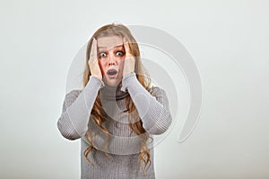 Woman in gray sweater holds her head with her hands from surprise fright shock