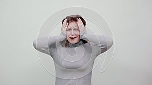 Woman in gray sweater holds her head with her hands from surprise fright shock