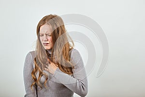 Woman in gray sweater with red hair feels pain in chest, touches the sore spot