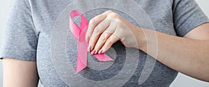 Woman in gray t-shirt attaches pink ribbon to her chest. Breast Cancer Awareness Month. Promoting campaign against