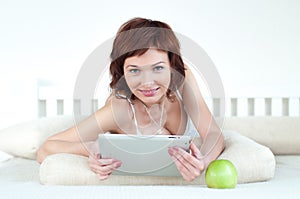 Woman with an green apple and tablet at bed reading ebook