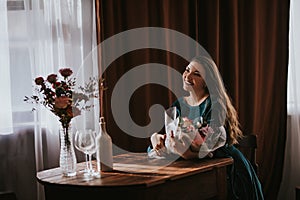 Woman in a green dress with a bouquet of flowers. Glass vase with flowers on a wooden table in front of a light background. On the