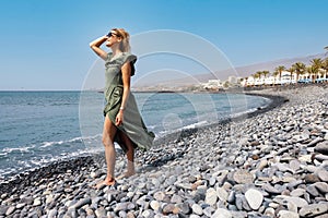 woman in green dress enjoying sun at rocky Playa de las Americas beach in Tenerife. Canary islands