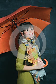 Woman in green dress holds leaves under orange umbrella