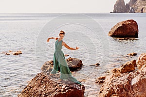 Woman green dress sea. Woman in a long mint dress posing on a beach with rocks on sunny day. Girl on the nature on blue