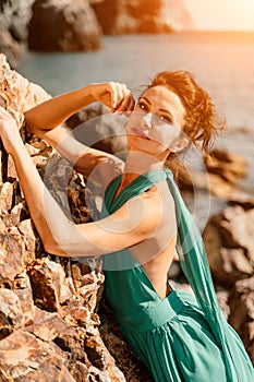 Woman green dress sea. Woman in a long mint dress posing on a beach with rocks on sunny day. Girl on the nature on blue