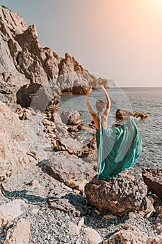 Woman green dress sea. Woman in a long mint dress posing on a beach with rocks on sunny day. Girl on the nature on blue