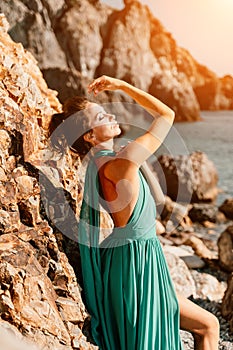 Woman green dress sea. Woman in a long mint dress posing on a beach with rocks on sunny day. Girl on the nature on blue