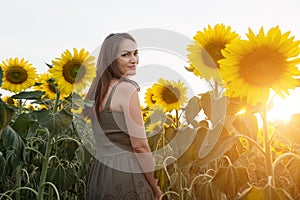 Woman in green dress walks across sunflowers on field