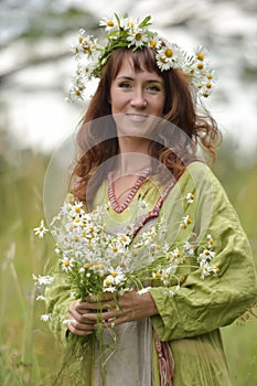 Woman in a green dress with a wreath of daisies in her hair and a bouquet of daisies in her hands