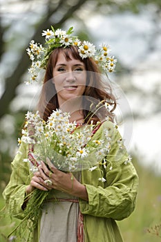 Woman in a green dress with a wreath of daisies in her hair and a bouquet of daisies in her hands