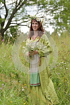 Woman in a green dress with a wreath of daisies in her hair and a bouquet of daisies in her hands