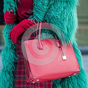 A woman in a green furry and warm fur coat in autumn or winter. Red burgundy bag. Fashionable bag close-up in female hands.