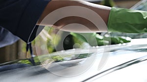 Woman in green gloves with a sponge wipes the car in the garden near the house in summer