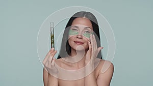 A woman with green hydrogel patches under her eyes holds a test tube with a plant. Seminude woman in the studio on a