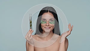 A woman with green hydrogel patches under her eyes holds a test tube with a plant. Seminude woman in the studio on a