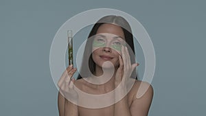 A woman with green hydrogel patches under her eyes holds a test tube with a plant. Seminude woman in the studio on a