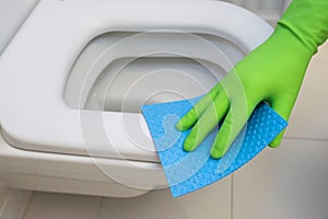 Woman in green rubber gloves cleaning toilet with blue cloth