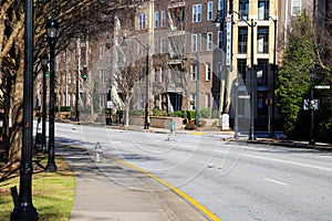 A woman in a green shirt crossing the street surrounded by brown apartment buildings with bare winter trees, lush green plants