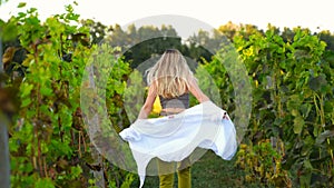 Woman in green shorts and a white shirt walks happily through the rows of vineyards